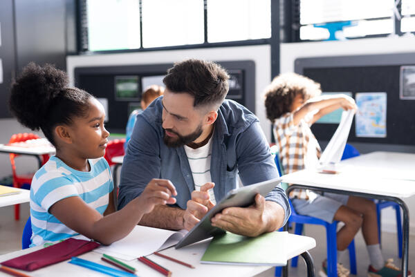 Diverse male teacher and schoolgirl using tablet at her desk in 