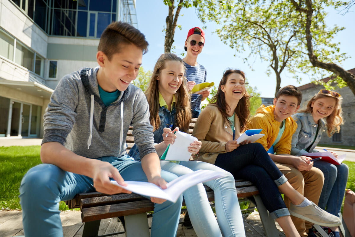 Bild vergrößern: Eine Gruppe Schüler sitzen vor einem Schulgebäude