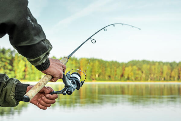 Hands of a man in a Urp plan hold a fishing rod, a fisherman catches fish at dawn. Fishing hobby vacation concept. Copy space.