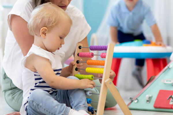 Kids playing on floor with educational toys in kindergarten. Children have fun in nursery or daycare. Babies with teacher in creche