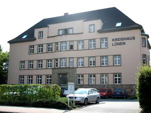 Bild vergr&ouml;&szlig;ern: Das Bild zeigt das Kreishaus in Lünen von der Straße aus gesehen. Ein großes Gebäude mit drei Stücken und vielen Fenstern mit einem kleinen Parkplatz davor und dunklen Dachziegeln.